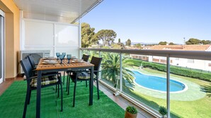 A balcony with a dining table, chairs, and a view of a swimming pool and greenery. - "Martin y Rose en Salou" Apartment with Sea View, Shared Pool and Wi-Fi (Salou)
