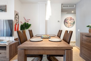 Un comedor con una mesa de madera, sillas, un televisor de pantalla plana y obras de arte en las paredes.