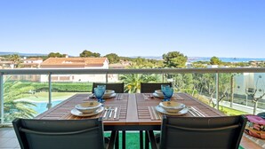 A balcony table set with plates, cutlery, and blue glassware, overlooking a residential area and a body of water. - "Martin y Rose en Salou" Apartment with Sea View, Shared Pool and Wi-Fi (Salou)