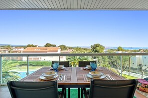 Une table de balcon, dressée avec des assiettes, des couverts et de la verrerie bleue, donnant sur un quartier résidentiel et un plan d’eau.