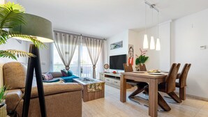 A modern living room with a sofa, coffee table, dining table, and chairs. There is a TV, a plant, and a lamp. - "Martin y Rose en Salou" Apartment with Sea View, Shared Pool and Wi-Fi (Salou)