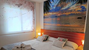 A hotel room with a bed, pillows, a nightstand, a lamp, a window with a view, and a wall mural. - "Martin y Rose en Salou" Apartment with Sea View, Shared Pool and Wi-Fi (Salou)
