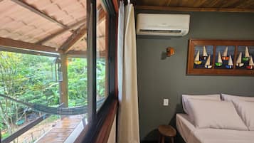 A room with a bed, a hammock, and a view of greenery outside.