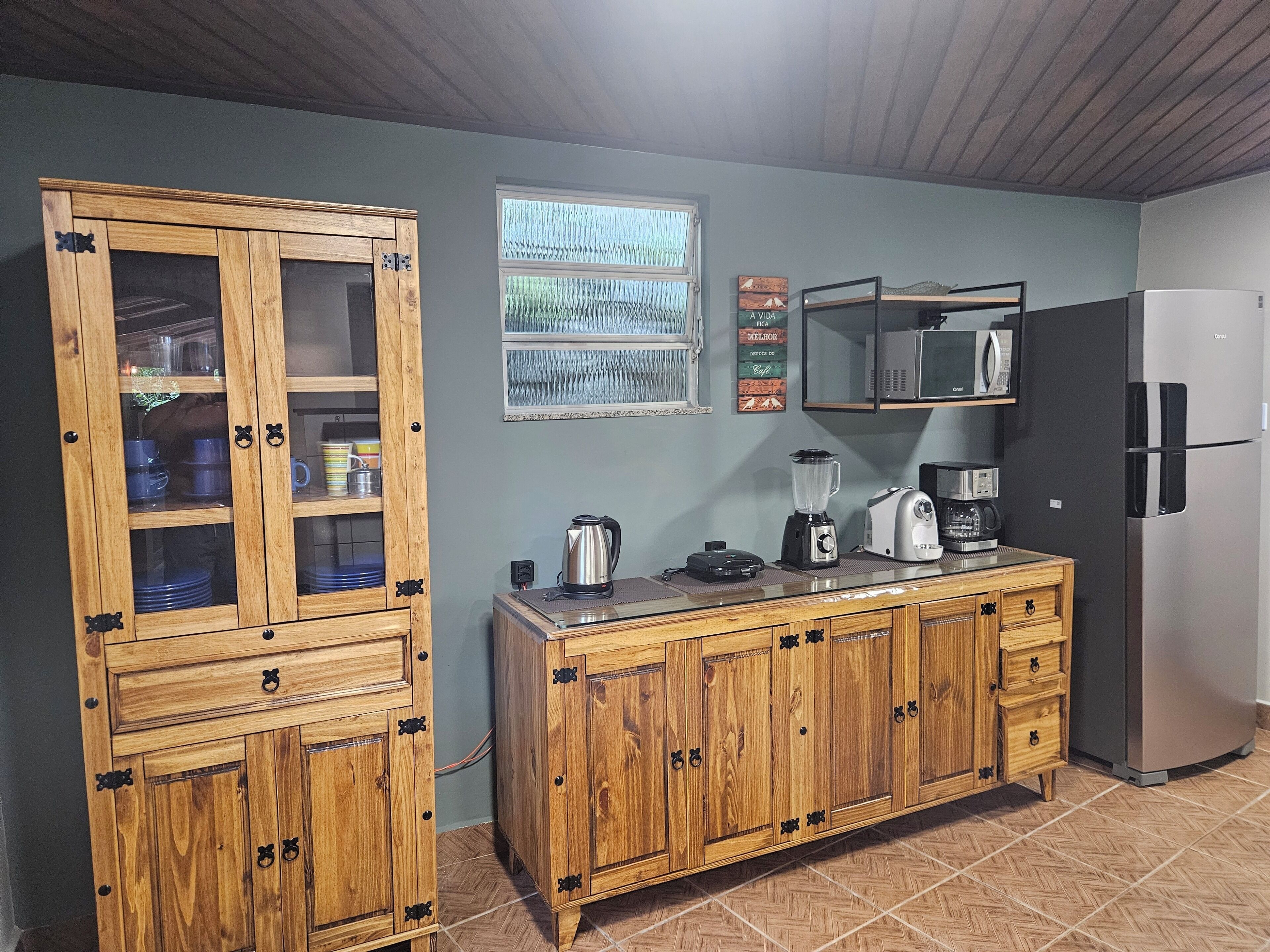 A kitchen with wooden cabinets, a refrigerator, a microwave, and a window with curtains.