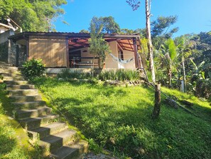 A house with a stone staircase leading to a wooden deck, surrounded by lush greenery and a clear blue sky. - Green Area House (Angra dos Reis)