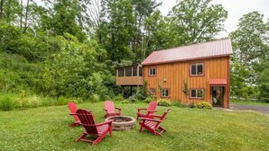 A wooden cabin with a metal roof, surrounded by a grassy yard with a fire pit and red Adirondack chairs. - Inn at High Falls (High Falls)