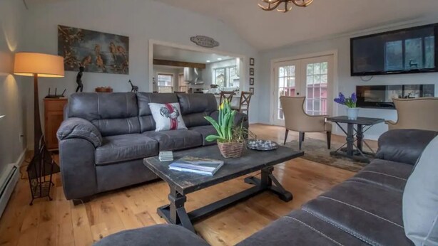 A spacious living room with a sofa, a coffee table, and a television. There is a dining area with a table and chairs visible in the background. - Inn at High Falls (High Falls)