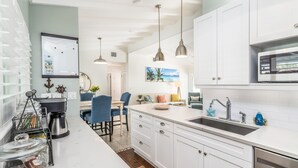 Una cocina moderna con gabinetes blancos, un lavamanos de acero inoxidable e iluminación colgante.