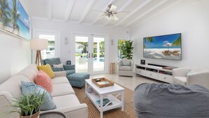 Amplia sala de estar con un sofá blanco, una mesa de centro y un mueble para la televisión. Cuenta con un ventilador de techo y un ventanal que proporciona luz natural.