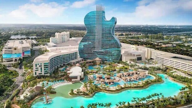 Un resort con un edificio con forma de guitarra, varias piscinas y exuberante jardinería.