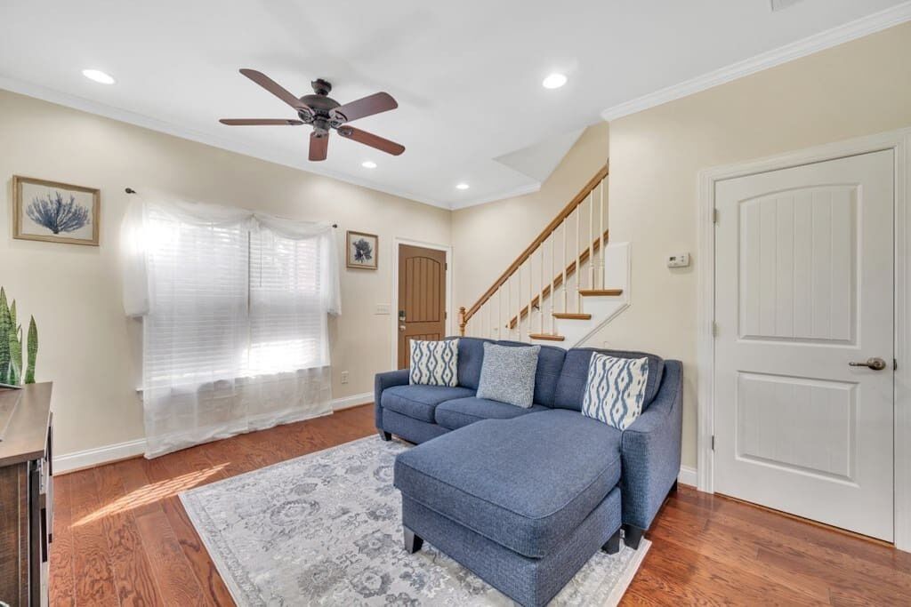 A living room with a sectional sofa, a ceiling fan, a staircase, and a door.