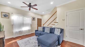 A living room with a sectional sofa, a ceiling fan, a staircase, and a door.