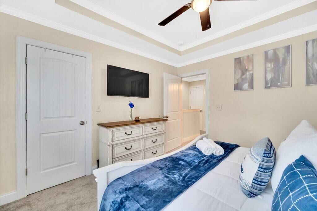Un dormitorio con cama, cómoda, ventilador de techo, televisor y obras de arte en las paredes.