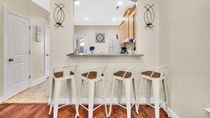 Una cocina con barra, taburetes blancos y un letrero en la pared.
