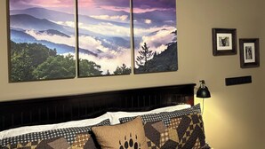 A bedroom with a bed, a headboard, a wall-mounted picture of a mountain landscape, and two framed pictures on the wall. - 2 BR, 1-1/2 bath house in wooded setting with private back yard, deck, hot tub. (Waynesville)
