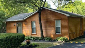 A log cabin with a number 7935 on the door, a small porch, and a well-maintained garden. - 2 BR, 1-1/2 bath house in wooded setting with private back yard, deck, hot tub. (Waynesville)