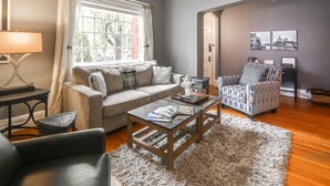 Ein Wohnzimmer mit einer Couch, einem Sessel, einem Couchtisch und einem Fenster mit Vorhängen.