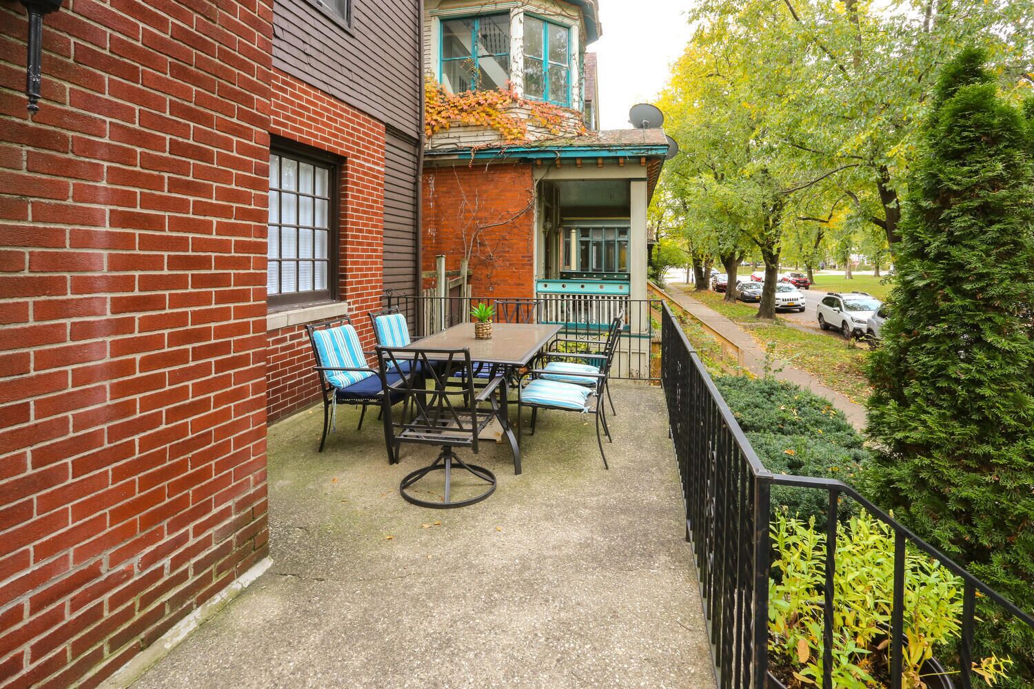 A patio with a table and chairs, a brick wall, and a view of a street with cars and trees.