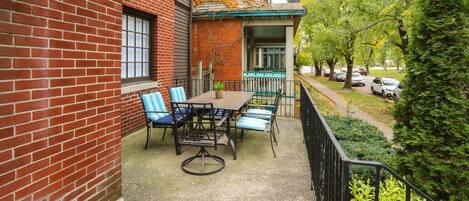 A patio with a table and chairs, a brick wall, and a view of a street with cars and trees.