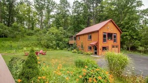 A wooden cabin with a red roof, surrounded by lush greenery and orange flowers.
