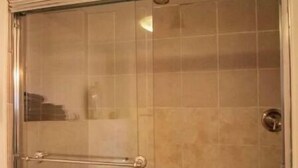A glass-enclosed shower with a metal handle and a white bathtub.