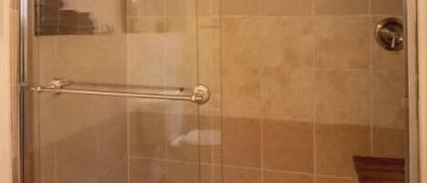 Una ducha con cerramiento de vidrio, un grifo de metal y una bañera blanca.