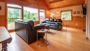 A cozy living room with two leather sofas, a wooden dining table, and large windows offering a view of the outdoors. - The Loft At The Inn At High Falls (High Falls)