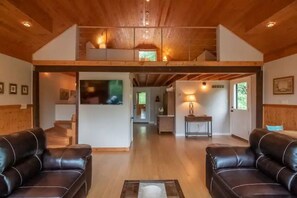 A spacious living area with a high ceiling, wooden beams, two leather sofas, a central rug, and a staircase leading to an upper level. - The Loft At The Inn At High Falls (High Falls)