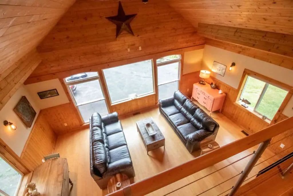 Ein gemütliches Blockhaus-Interieur mit Holzbalkendecke, einer Sterndeko, einer Sofagarnitur, einem kleinen Tisch und einem pinken Schrank.