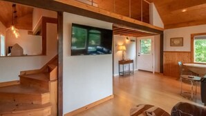 A spacious room with a wooden staircase, a large window, and a dining area. - The Loft At The Inn At High Falls (High Falls)