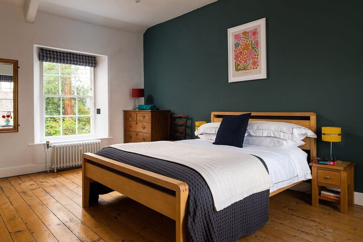 Une chambre à coucher avec un lit en bois, une fenêtre donnant sur un paysage verdoyant, une commode et une table de chevet avec une lampe.