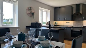 A modern kitchen with dark cabinets, a microwave, and an oven. There is a dining area with a table set for four, including plates, bowls, and glasses. - The Mariners' Beacon Torquay (Torquay)