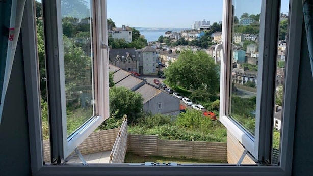 A view through an open window of a residential area with houses, a road, and a body of water in the distance. - The Mariners' Beacon Torquay (Torquay)