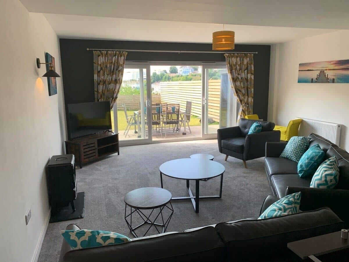 A living room with a sofa, two coffee tables, a TV, and a sliding glass door leading to an outdoor area with a table and chairs.