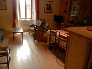 Un salon chaleureux avec un plancher en bois, une table à manger, un téléviseur et un coin cuisine équipé de placards.