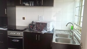 A kitchen with dark cabinets, a stove, an oven, a sink, and a window with blinds. - Spacious Serviced Apartments in Owerri,Accommodation Corporate and Private Stays (Owerri)