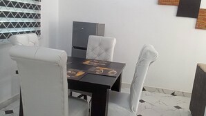 A dining area with a table set for four, surrounded by white upholstered chairs. - Spacious Serviced Apartments in Owerri,Accommodation Corporate and Private Stays (Owerri)