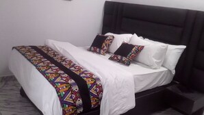 A neatly made bed with a patterned bedspread and pillows, a black headboard, and a white wall. - Spacious Serviced Apartments in Owerri,Accommodation Corporate and Private Stays (Owerri)