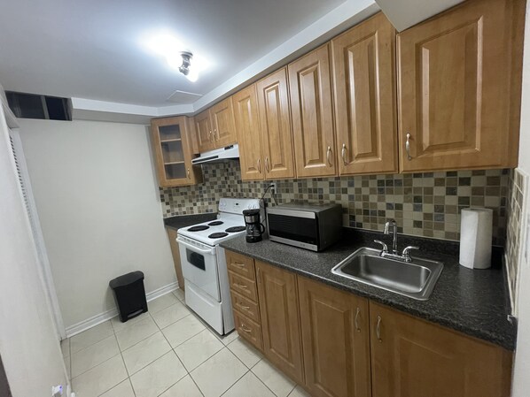 A compact kitchen with wooden cabinets, a stove, a microwave, and a sink.