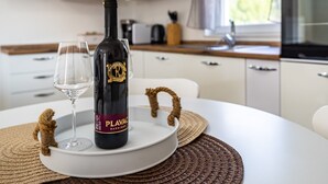 Eine Flasche Plavac Barrique Wein, ein Weinglas und ein rustikaler Seilgriff auf einem weißen Tisch mit einer gewebten Tischmatte.