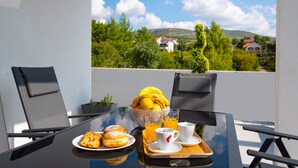 Ein Tisch mit Frühstücksangeboten, ein Glas Orangensaft und Blick auf eine grüne Landschaft mit Häusern.