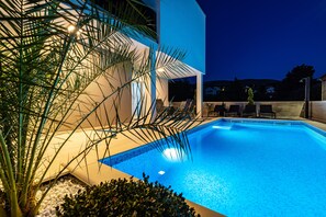Une piscine à l’eau d’un bleu cristallin, entourée de petits galets blancs et de plantes tropicales.