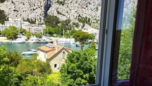 Vista desde una ventana sobre un puerto deportivo con barcos, una montaña rocosa y edificios al fondo.