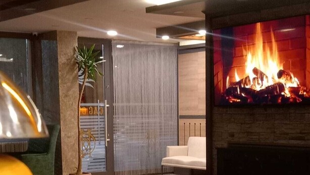 A modern interior with a fireplace, seating area, and a bar counter with a drink. - Çag Otel (Erzurum)