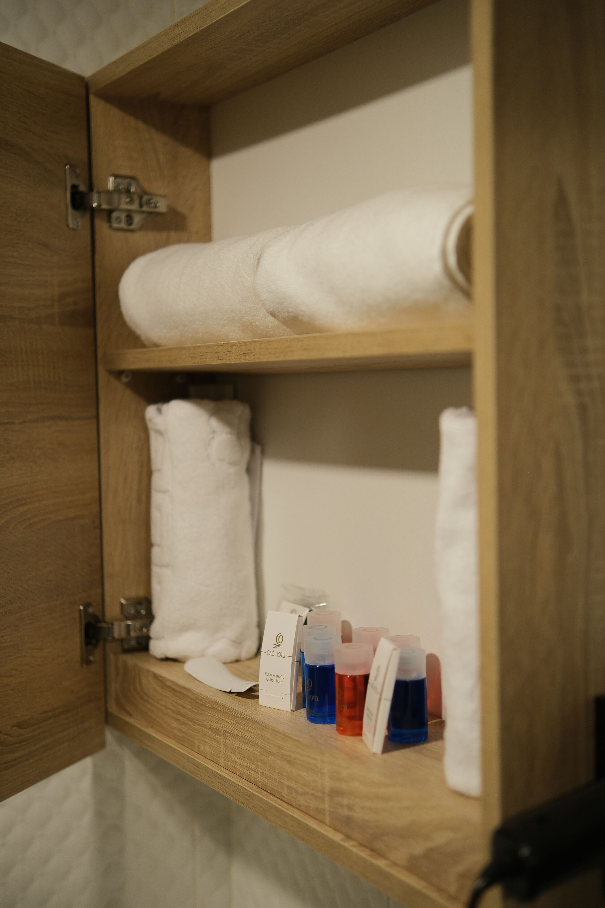En træhylde med hvide håndklæder og toiletartikler i et badeværelse.