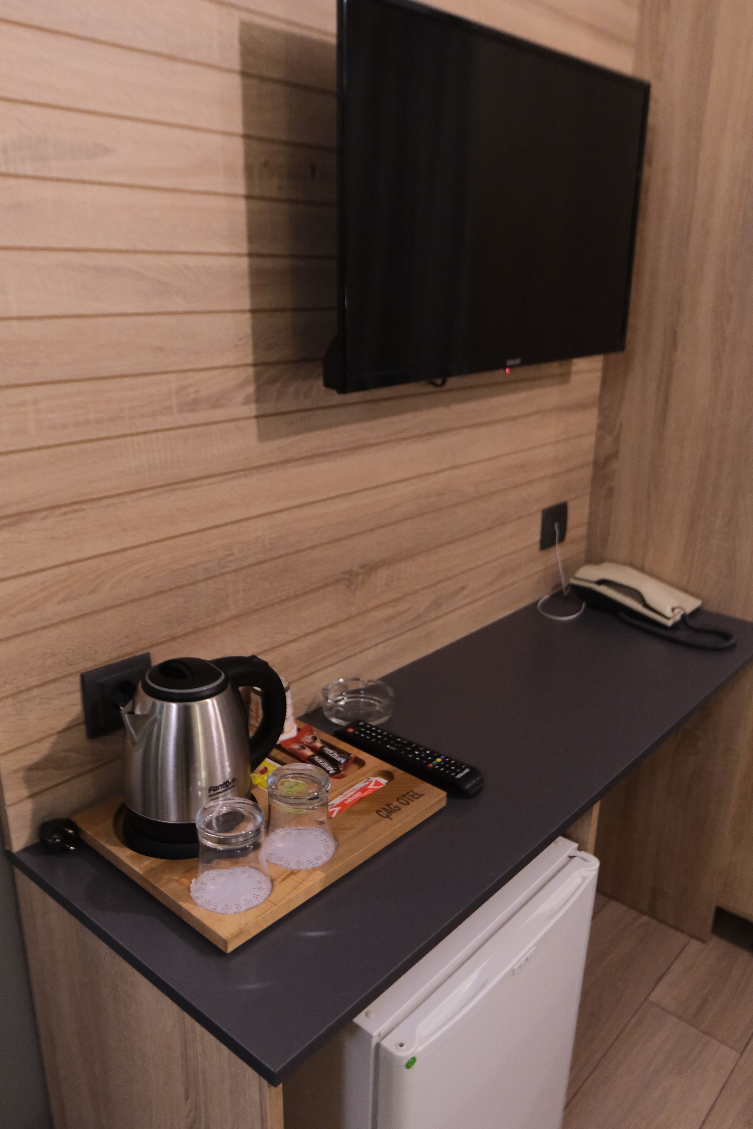Uma cozinha compacta com bancada de madeira, chaleira, copos, um controle remoto e um telefone pendurado.