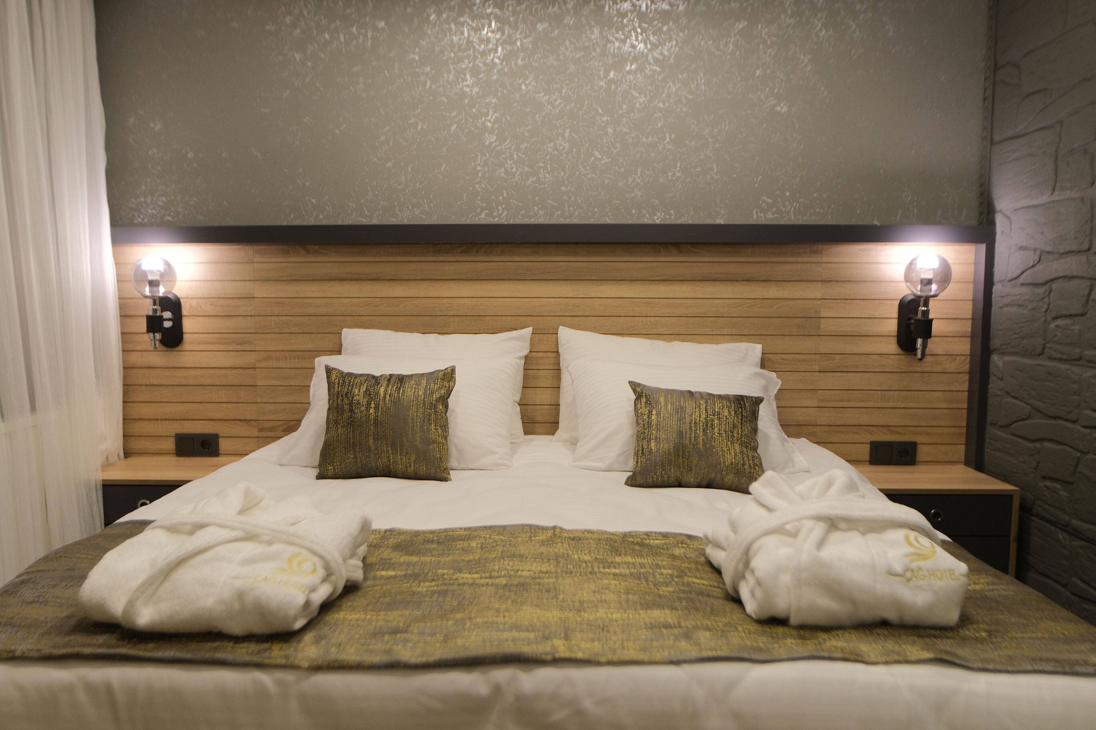 A neatly made bed with white linens, two gold pillows, and two white towels folded at the foot of the bed.