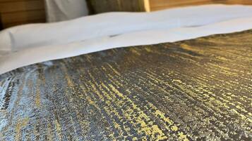 Una cama con una colcha dorada y negra de textura, un cabecero de madera y una lámpara fijada a la pared.