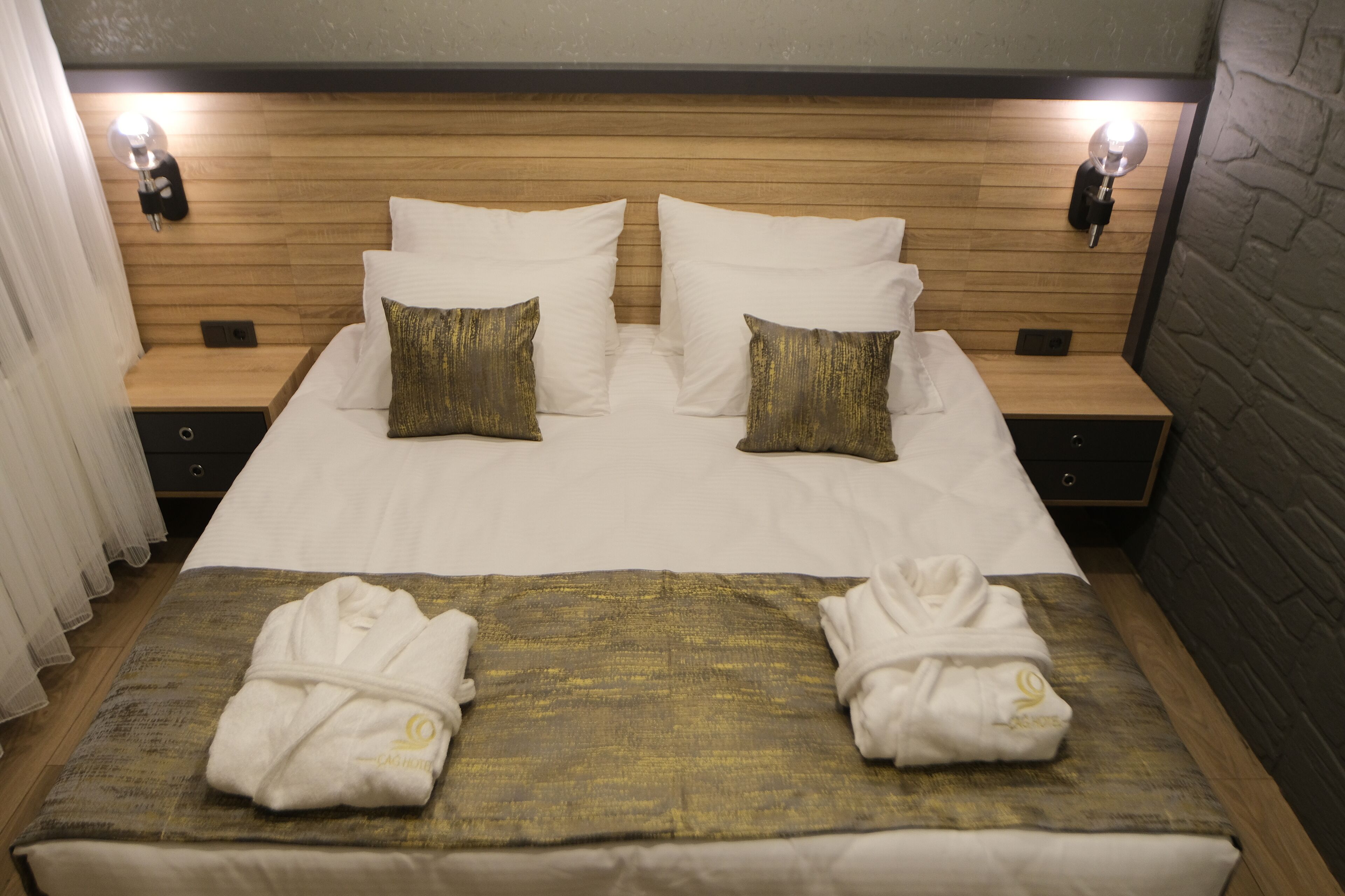 Une chambre d’hôtel avec une tête de lit en bois, deux tables de chevet et un lit avec une literie blanche et des oreillers dorés.