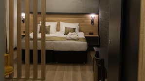 A modern bedroom with a wooden headboard, a bed with white linens, a nightstand with a lamp, and a wooden floor. - Çag Otel (Erzurum)